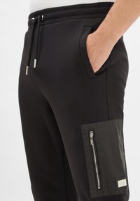 Zwarte joggingsbroek met een zachte textuur, voorzien van een elastische tailleband, zijzakken en een ritszak op het onderbeen met een logo-accent.