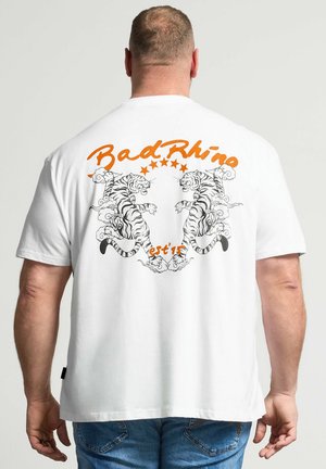 Mand iført hvid T-shirt med orange "Bad Rhino" tekst og to brølgende tigre, der vender mod hinanden på ryggen.