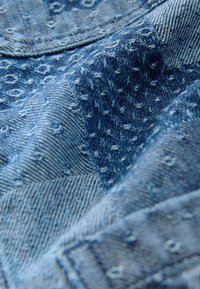 Tissu en denim de différentes nuances de bleu, présentant un motif texturé avec des points en relief et des rayures diagonales. Texture douce et tissée avec des coutures visibles.