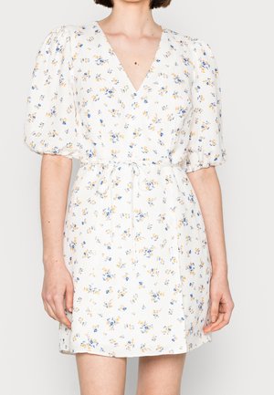 Biała sukienka w kwiaty z głębokim dekoltem w kształcie litery V, bufkami na rękawach i wiązaniem w talii. Ozdobiona nadrukiem drobnych niebieskich i żółtych kwiatów na jasnym tle.