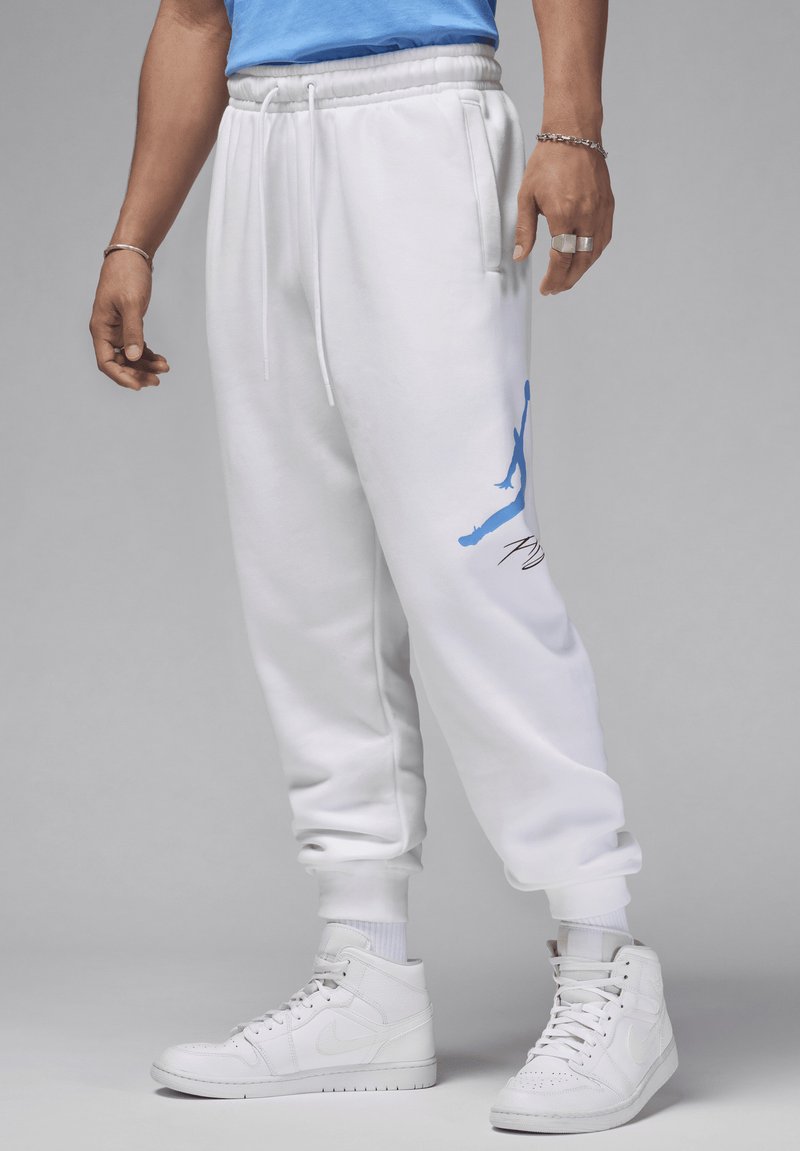 Weiße Jogginghose mit elastischem Bund, Kordelzug und Seitentaschen. Mit einem blauen Jumpman-Logo am linken Bein. Kombiniert mit weißen Sneakers.
