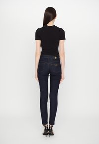 Svart åtsittande t-shirt, mörka denim skinny jeans, synliga bakfickor, guldtråd som accent, och svarta högklackade skor.