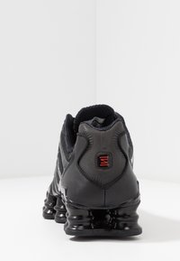 Μαύρο αθλητικό παπούτσι με επάνω μέρος από υλικό συνθετικού πλέγματος με υφή, μαξιλαρωμένο γιακά και ορατή μαύρη λαστιχένια σόλα με ξεχωριστά στοιχεία απορρόφησης κραδασμών. Λογότυπο με κόκκινες λεπτομέρειες.