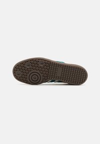 Brown rubber sneaker sole featuring a textured grip pattern, circular details, and teal accents on the side, with a durable, foot-shaped design.