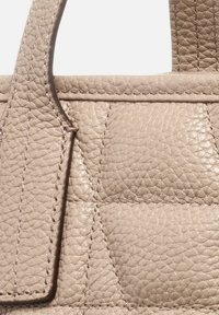 Borsa a manico corto in pelle beige con design trapuntato, caratterizzata da dettagli cuciti e texture liscia. I manici corti ne migliorano la funzionalità.