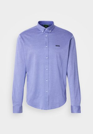 Camisa de botão de manga longa em púrpura claro, feita de tecido texturizado. Apresenta um colarinho, punhos e um logotipo preto bordado no peito.