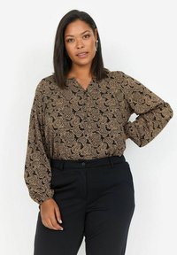 Schwarze Bluse mit einem beigen Paisleymuster, ausgestattet mit langen Ärmeln und einem V-Ausschnitt, kombiniert mit schwarzen Hosen. Glatte Stofftextur.