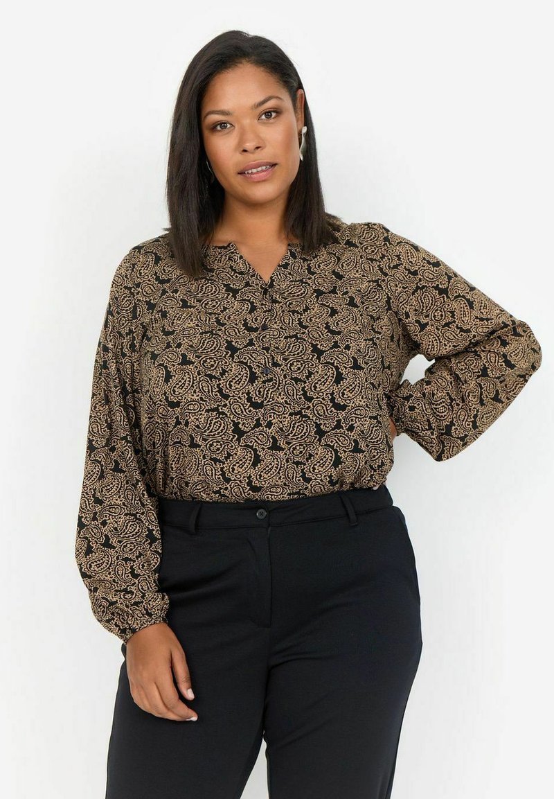 Schwarze Bluse mit einem beigen Paisleymuster, ausgestattet mit langen Ärmeln und einem V-Ausschnitt, kombiniert mit schwarzen Hosen. Glatte Stofftextur.