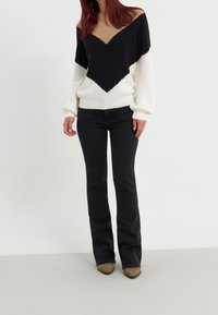 Sweter dziany z wzorem jodełki w kolorach beżowym, czarnym i białym; zestawiony z dopasowanymi czarnymi dżinsami i jasnobrązowymi szpilkami.