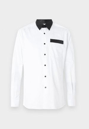 Balta garām piedurknēm krekls ar melnu apkakli un kabatu. Priekšpusē ir plastmasas melni pogas un uz kabatas. Gluda tekstūra.