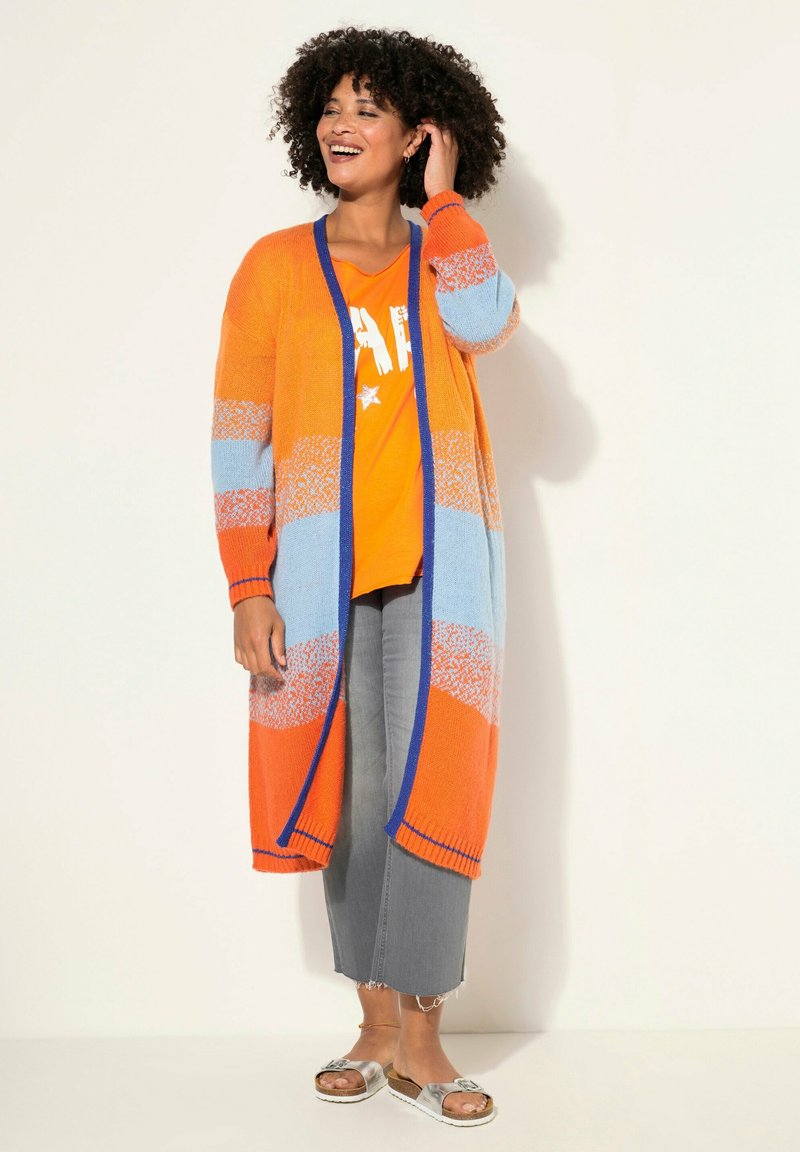 Jersey largo en rayas naranjas, azules y blancas, con un pronunciado escote en V, puños acanalados y abierto por delante. Combinado con una camiseta naranja brillante.