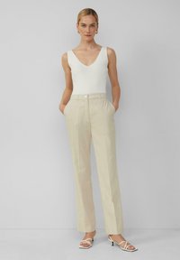 Witte mouwloze top met een diepe V-hals, gecombineerd met lichtbeige, gestructureerde wijde broek met opgestikte zakken en een knoopsluiting.