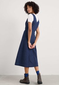 Midihame denim, tummansininen, jossa on istuva yläosa ja leveä helma. V-oikoinen selkäosa, käytetty valkoisen istuvan paidan ja ruskeiden nilkkabootsien päällä.