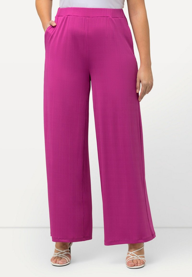 Femme portant un pantalon large magenta vif avec taille élastique et poches latérales, associé à des sandales blanches à brides et à bout ouvert.