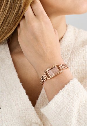 Roosa kuldne metallkäevõru koos ristkülikukujulise kellanäidikuga, millel on tekstureeritud roosakas taust. Ahelakujuline disain koos sileda riistvara aktsendiga.