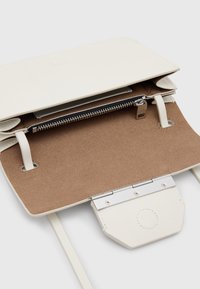 Lys beige læder crossover taske med en glat overflade, klaplukning og en brun ruskind indvendig med en lynlås lomme. Sølv hardware detaljer.