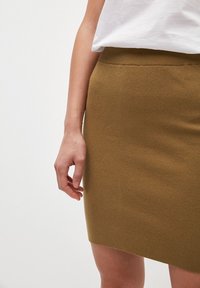 Gonna in maglia verde oliva con un tessuto testurizzato, dotata di una cintura morbida e di una forma aderente, parzialmente visibile sopra il ginocchio.