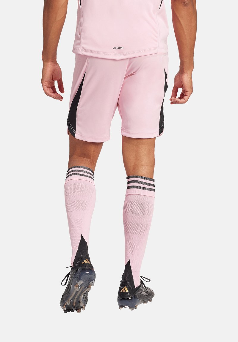 Rosa Fußballuniform mit schwarzen Akzenten, bestehend aus einem kurzärmeligen Oberteil und Shorts. Schwarze und weiße gestreifte Kniestrümpfe und schwarze Fußballschuhe.
