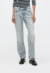 Svetlo modré denimové džínsy s rovn�ým strihom, so zosvetlenou textúrou, piatimi vreckami a pútkami na opasok. Nosené s prúžkovaným čiernym a bielym topom.