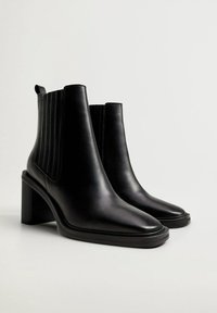 Stivali ankle in pelle nera con punta affusolata, pannelli laterali testurizzati e tacco a blocco. Finitura liscia con dettagli di cucitura sottili.