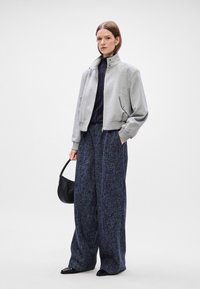 Grijze korte bomberjack met hoge kraag, gecombineerd met losse, navy textuur brede broek en een kleine zwarte handtas.