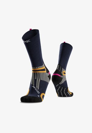 Chaussettes de sport bleu foncé avec des accents gris, jaunes et roses, montrant les étiquettes des pieds gauche et droit, posées sur fond blanc.