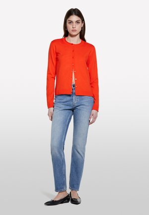 Roter Cardigan aus Strickmaterial mit rundem Ausschnitt. Er verfügt über eine knöpfbare Vorderseite und lange Ärmel, kombiniert mit hellblauen Jeans.