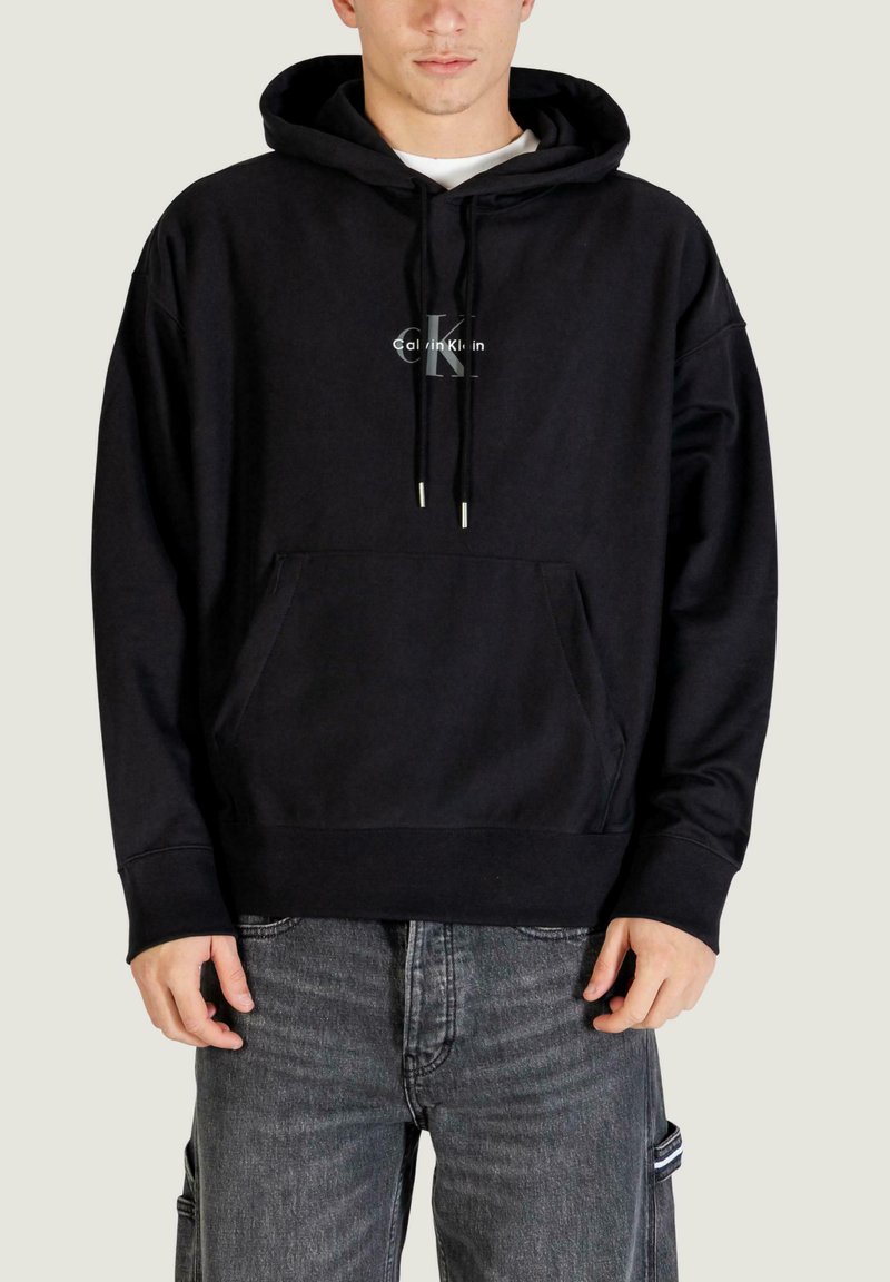 Sudadera negra con capucha hecha de tela suave, con un bolsillo frontal, detalles de cordón y un gráfico del logo en el centro.