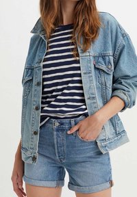 Chaqueta vaquera en azul claro con cierre de botones, combinada con una camiseta a rayas azul marino y blanca y pantalones cortos vaqueros azules remangados.