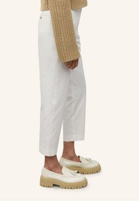 Pantalons blancs coupés en denim, avec une coupe droite. Associés à des mocassins crème à semelle épaisse et avec des franges décoratives.