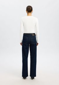 Temno modre široke kavbojke z visokim pasom, oblikovane s petimi žepi in kontrastnim šivom, v kombinaciji z oprijetim belim dolgim rokavom.