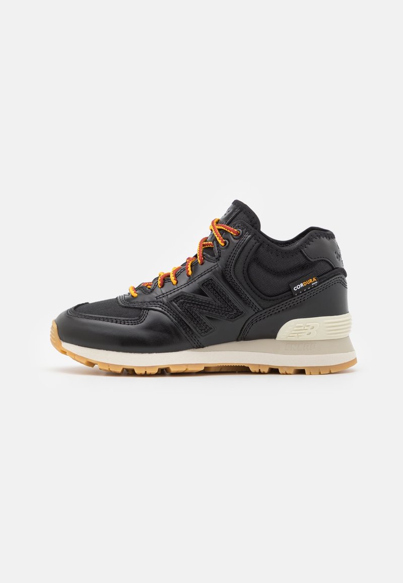 Zwarte sportieve schoenen met een gestructureerde leren bovenkant, oranje veters en een gumrubberen buitenzool. Bevat een opvallende zijlogo-detail.
