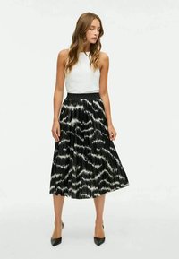 Melnbalta svārku ar krokām, kam ir viļņaina raksts, augsta josta, apvienota ar baltu bezpiedurkņu topu un melniem norādītājiem zābakiem.