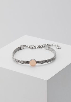 Bracelet en maille argentée avec un pendentif rond en or rose sur un socle blanc, doté d'un fermoir mousqueton et d'une chaîne réglable.
