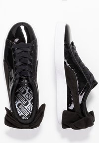 Sneaker in pelle verniciata nera e suede con suola bianca. Presenta una superficie testurizzata, lacci piatti e una fodera interna a motivo.