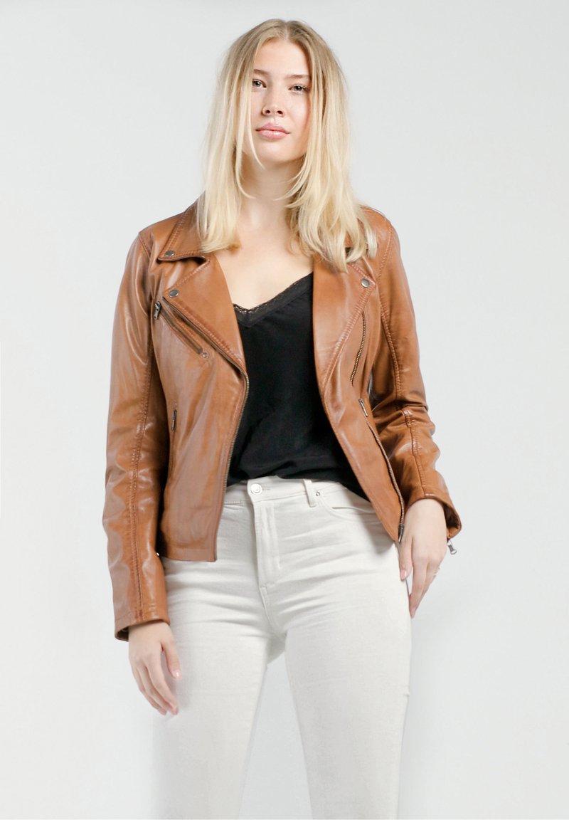 Bruine leren motorjack met een asymmetrische rits, een reverskraag en lange mouwen, gecombineerd met een zwart topje en lichtgekleurde jeans.