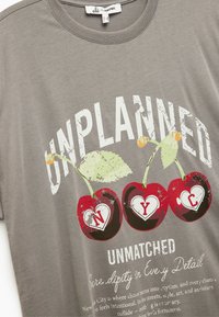 Szary bawełnowy t-shirt z graficznym nadrukiem przedstawiającym dwie wiśnie oraz napisem "UNPLANNED UNMATCHED NYC" w kontrastowych kolorach.