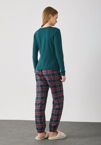 Langærmet teal top med rund halsudskæring, der er parret med grønne og røde ternede pyjamasbukser, der har elastisk talje og manchetter ved anklerne.