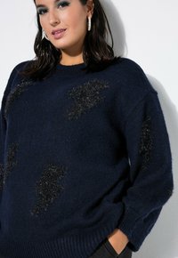 Marineblauwe gebreide trui met losse pasvorm, voorzien van zachte zwarte bliksempatroon. Geribbelde manchetten en zoom voegen textuur toe.