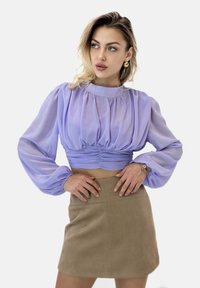 Top corto a maniche puff in lavanda con dettaglio in vita arricciata, abbinato a una mini gonna in suede beige con una texture liscia e linee pulite.