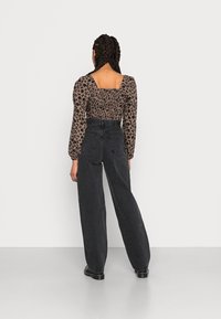 Paita kuosi leopardi, pitkät hihat ja neliskanttinen kaula-aukko, yhdistetty korkeavyötäröisiin, löysän mallisiin mustiin farkkuihin, joissa on näkyvät saumat ja taskut.