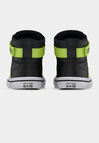 Μαύρα και νέον πράσινα ψηλά παπούτσια Converse All Star, φαίνονται από πίσω, με λευκές σόλες και λογότυπο στη φτέρνα.