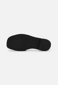 Black rubber shoe sole with a textured surface, round toe, and heel. Marked with "DKNY" on the side. Flat profile, no patterns or accents.