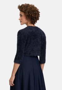 Veste cropped bleu marine avec une texture duveteuse, manches trois-quarts et col rond, associée à une jupe fluide bleu marine.