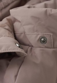 Šviesiai rožinė pamušta striukė su matinio paviršiaus audiniu, sidabriniais spaudės mygtukais ir subtilia siuvimo detalėmis, pabrėžianti švelnų, izoliuotą dizainą.