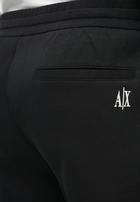 Čierne tepláky s jemnou textúrou, so zadnou vreckom a bielym vyšitým logom "A/X". Elastický pás pre pohodlie.