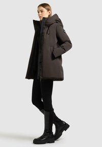 Giubbotto trapuntato nero con colletto alto, zip frontale, tasche laterali e una texture liscia. Indossato con leggings neri e stivali al ginocchio.