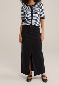 Randig marinblå och vit kortärmad skjorttröja i knäppning, kombinerad med en svart denim maxikjol med en framsläppt slits. Bärs med leopardmönstrade flats.