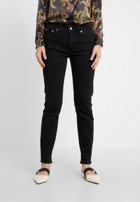 Jeans negros ajustados con una textura suave, diseño de cinco bolsillos y herrajes plateados, combinados con una blusa de manga larga estampada y zapatos planos puntiagudos.