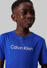 T-shirt di cotone blu con maniche corte, caratterizzato da un logo bianco "Calvin Klein" sul davanti. Tessuto liscio con scollatura a girocollo.